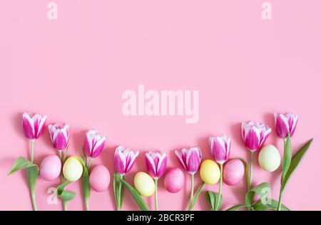 Schöner Oster-Rahmen mit Tulpen und Eiern auf pinkfarbenem Hintergrund. Frohes Osterkonzept. Kopierbereich, Draufsicht, flaches Layout. Stockfoto