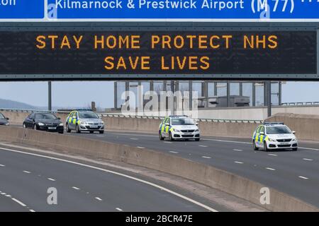 Coronavirus UK - Maßnahmen in Schottland - Polizeifahrzeuge, die unter dem Schild "Day Home Protect NHS Save Lives" in Glasgow fahren Stockfoto