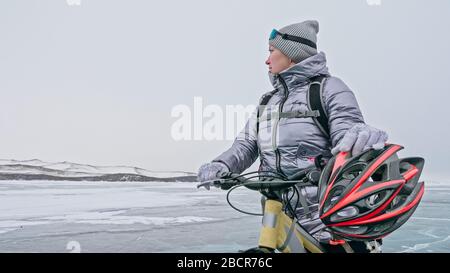 Frau steht in der Nähe ihres Fahrrads auf Eis. Die Radfahrerin hörte auf zu r Stockfoto