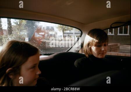 Eine junge Mutter blickt herab, mit ihrer jungen Tochter, die auf dem hinteren Beifahrersitz eines Alfa Romeo 2000 GTV-Wagens sitzt, der vor einem Restaurant in den Vororten von London, Großbritannien 1974, geparkt wurde Stockfoto