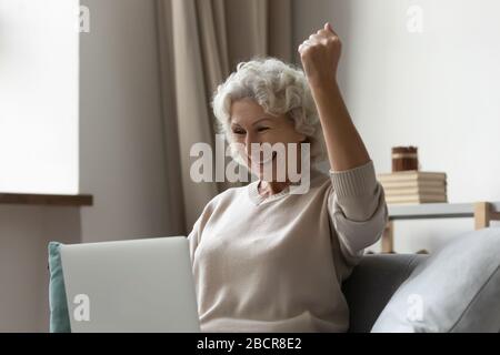 Überfreute ältere Seniorin mit Blick auf den Laptop-Bildschirm, die Erfolge feiern. Stockfoto