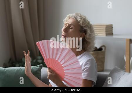 Gestresste Rentnerin mittleren Alters mit Papierfan. Stockfoto