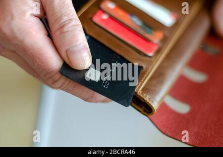 Hand nimmt eine Bankkarte aus der Geldbörse. Erwachsener hält eine schwarze Bankkarte. Zahlung für Waren im Laden. Selektiver Fokus. Nahaufnahme. Stockfoto