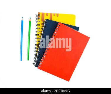 Blaue und grün gefärbte Bleistiftkrebse aus Holz, die neben drei verschiedenfarbigen Notizbüchern auf weißem Hintergrund platziert sind Stockfoto