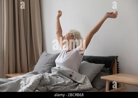 Glückliche, emotionale, im mittleren Alter gezogene Frau, die sich nach dem Aufwachen zurückstreckt. Stockfoto