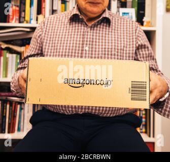 Paris, Frankreich - 2. April 2019: Glücklicher älterer Mann, der im Wohnzimmer ein neues Paket von der E-Commerce-Website von Amazon Prime Japan im Online-Shop Amazon.co.jp hält Stockfoto