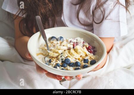 Über Nacht Haferbrei mit Beeren, Bananen, Marmelade und Kokosnuss in weißer Schüssel in den Händen. Stockfoto