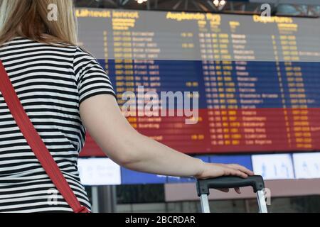 Frau schaut auf die Anzeigetafel am Flughafen. Wählen Sie ein Land für Reisen oder Migration aus. Stockfoto