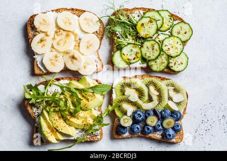 Gesundes Frühstück Toast. Vollkornkröten mit Frischkäse, Früchten, Beeren und Honig, gesalzene Toasts mit Avocado und Gurke. Veganes Lebensmittelkonzept Stockfoto