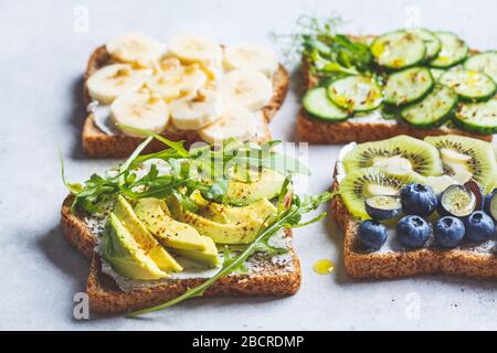 Gesundes Frühstück Toast. Vollkornkröten mit Frischkäse, Früchten, Beeren und Honig, gesalzene Toasts mit Avocado und Gurke. Veganes Lebensmittelkonzept Stockfoto