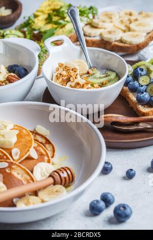 Gesunder, abwechslungsreicher vegetarischer Frühstückstisch. Haferbrei mit Obst, chia Pudding, Pfannkuchen mit Bananen und Honig und Toast mit Obst, Gemüse und cr Stockfoto