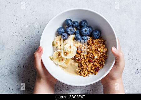 Granola mit Beeren und Früchten in einer weißen Schüssel auf grauem Grund. Gesundes Frühstückskonzept. Stockfoto