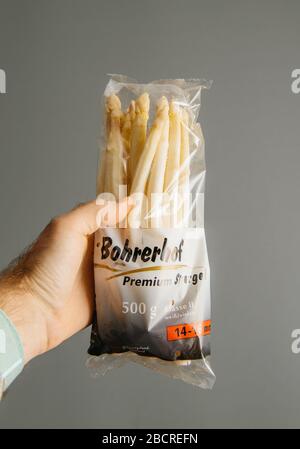 Paris, Frankreich - 14. April 2019: Männliche Hand hält vor grauem Hintergrund frische Premium deutsche Spargel vom Bohrerhof Stockfoto