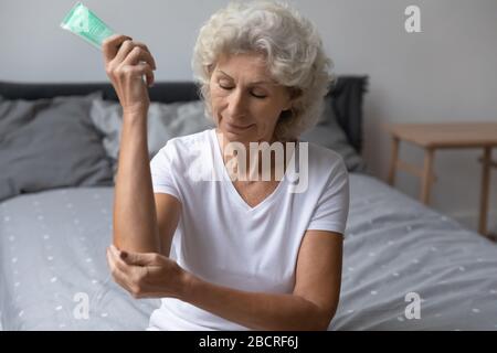 Glückliche Frau mittleren Alters, die feuchtigkeitsspendende Creme auf der Ellenbogenhaut anwendet. Stockfoto