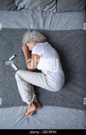 Gestresste Frau im Ruhestand, die in fetaler Position auf dem Bett liegt. Stockfoto