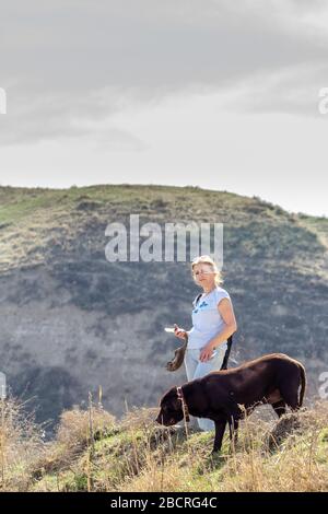 Frau im Freien mit einem Hund Labrador Retriever mit Mountain View und Smartphone in den Händen Stockfoto