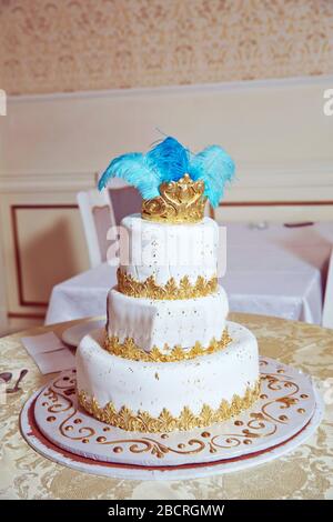 Der Kuchen hat blaue Federn und eine goldene Krone. Weißer dreifach gestufter Kuchen. Stockfoto