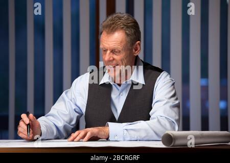 Lächelnder Architekt oder Ingenieur, der abends oder nachts in einem Büro arbeitet Stockfoto