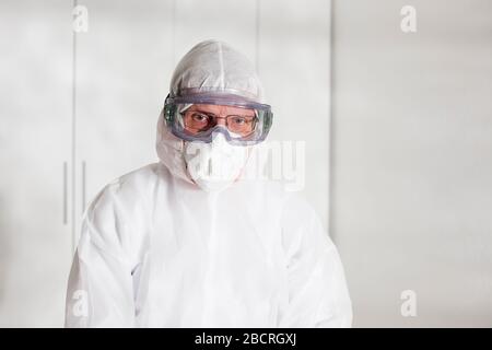 Depressiver Arzt mit weißer Schutzkleidung, der leider wegen der Probleme mit Kovid-19 aussieht Stockfoto