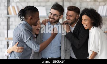 Stehen und umarmen lächelndes Team, das lachen, sich gegenseitig zu betrachten. Stockfoto