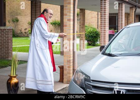 Houston, Texas, USA. April 2020. Pater TOM SMITHSON begrüßt die Gemeindemitglieder, da er an der Verteilung von Palmen in einem Drive-by-Vertrieb am Palmsonntag in der Corpus Christi Catholic Church Sunday, 5. April 2020, in Houston, Texas teilnimmt. Gutschrift: Lynn Pennington/ZUMA Wire/Alamy Live News Stockfoto