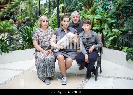 Porträt der kaukasischen Familie von der Mutter mit neugeborenem Baby und Sohn der Kinder, Großeltern. Auf der Bank sitzen Stockfoto