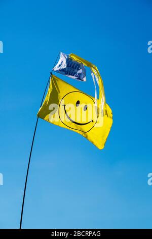 Gelbe Fahne mit Smiley-Symbol auf Teleskop-Anzeigestange, mit Windbock und Markierung "Ring laufen". Alles vor blauem Himmel. Stockfoto