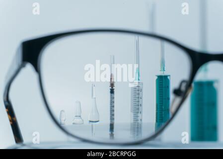 Blick in Brille. Medizin, Injektion, Impfstoff und Einwegspritze isoliert, Wirkstoffkonzept. Sterile Fläschchen medizinisch. Makro-Nahaufnahme auf Hintergründen grau. Stockfoto