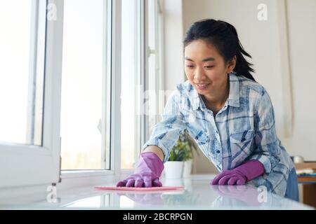 Porträt der jungen asiatischen Frau, die Fenster waschen und glücklich lächeln, während sie die Frühlingsreinigung genießen, Kopieraum Stockfoto