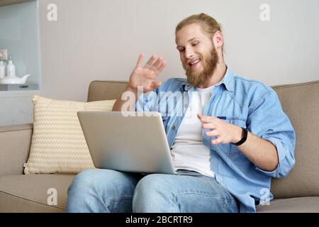 Happy Young man Video Telefonieren auf dem Laptop sitzen auf dem Sofa arbeiten von zu Hause aus. Stockfoto