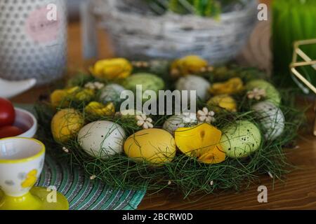 Osterkranz aus gefärbten Eiern. Dekorative Holzblumen auf dem Tisch. Stockfoto