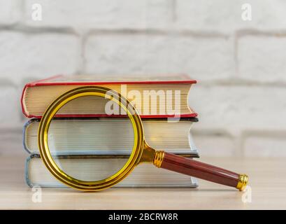 Ein Stapel Bücher und eine Lupe auf dem Tisch. Das Konzept des Informationsabrufs. Stockfoto