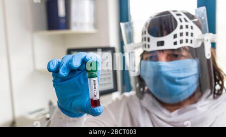 Reagenzglas. Positives Ergebnis: SARS-COV-2-Blutprobe in der Hand des Laborassistenten. Weibliches Sanitäter. Gesichtsschutzmaske oder -Abschirmung. COVID-19-Diagnostiklabor. Stockfoto