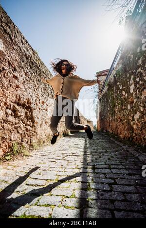 Junge Frau springt mit Glück zwischen historischen Wänden auf einer schmalen Gasse. Tourismus- und Reisekonzept Stockfoto