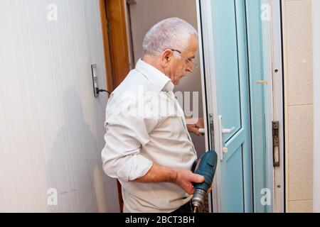 Der Mann installiert den Türgriff mit einem Bohrer. Reparaturarbeiten. Wartung in der Wohnung. Mann bohrt ein Loch in einer Tür . Mann bohrt ein Loch in A. Stockfoto