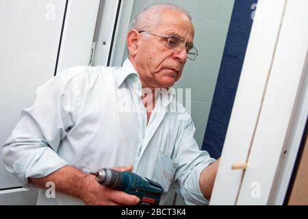 Der Mann installiert den Türgriff mit einem Bohrer. Reparaturarbeiten. Wartung in der Wohnung. Mann bohrt ein Loch in einer Tür . Mann bohrt ein Loch in A. Stockfoto