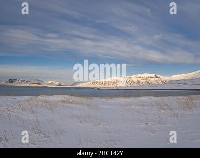 Eine verschneite Wiese an der Küste Islands mit Bergen im Hintergrund Stockfoto