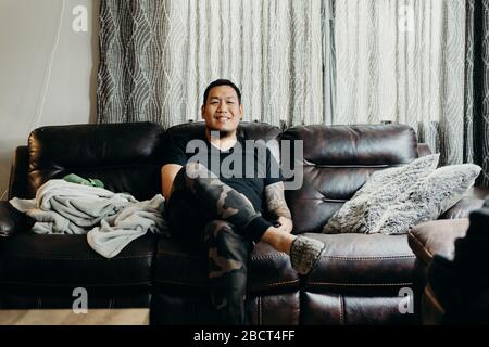 Asiatische bärtige Mann sitzen auf Couch im Wohnzimmer zu Hause. Smiley Gesicht. Stockfoto