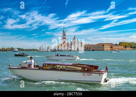 Ein Wassertaxi fährt über das Markusplatz mit der Kirche San Giorgio Maggiore und dem Glockenturm im Hintergrund, Venedig, Italien Stockfoto