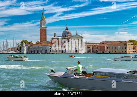 Ein Wassertaxi fährt über das Markusplatz mit der Kirche San Giorgio Maggiore und dem Glockenturm im Hintergrund, Venedig, Italien Stockfoto