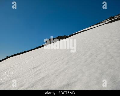 Ein Berghang in Island mit vulkanischem Gestein und glänzendem Schnee Stockfoto