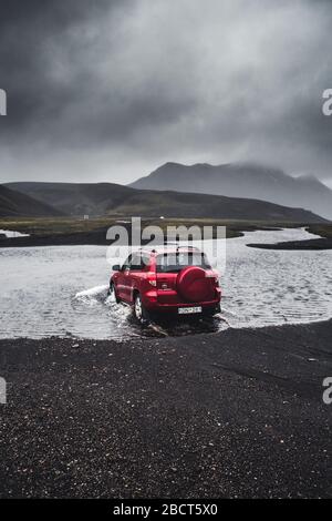 Highlands of Iceland - 07.08.2019: Rotes Auto über den Fluss in Landmannalaugar, Island. Geländewagen auf der Straße. Stockfoto