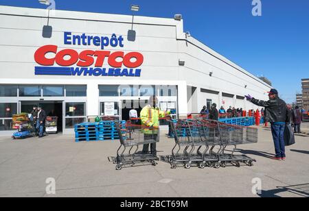 Montreal, Kanada - 4. April. 2020: Menschen mit Masken in einer Linie, um Costco Großhandel zu betreten. Viele Geschäfte führten soziale Distanzierungen durch, die zu Linien führten Stockfoto