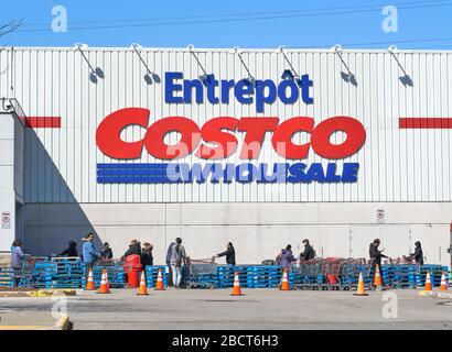 Montreal, Kanada - 4. April. 2020: Menschen mit Masken in einer Linie, um Costco Großhandel zu betreten. Viele Geschäfte führten soziale Distanzierungen durch, die zu Linien führten Stockfoto