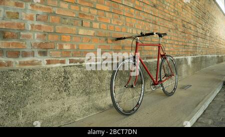 Retro-gestyltes, rotes, singlespeed, festes Zahnrad, isoliert an einer Ziegelwand Stockfoto