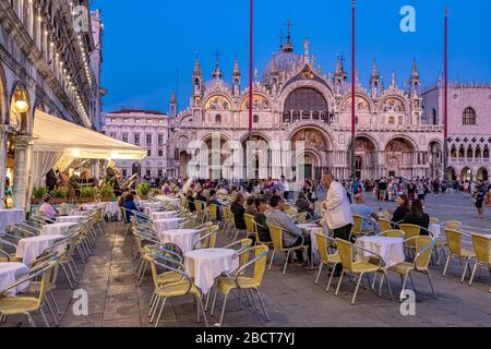 Leute, die vor der Lavena sitzen und am frühen Abend auf dem Markusplatz mit der Markusbasilika im Hintergrund, Venedig Caffè, Italien, einen Drink genießen Stockfoto