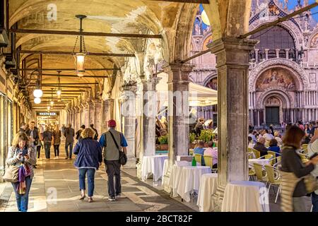 Menschen, die an Caffe Lavena vorbeigehen, genießen einen frühen Abendspaziergang durch die Portikus und Torbögen rund um den Markusplatz, Venedig, Italien Stockfoto