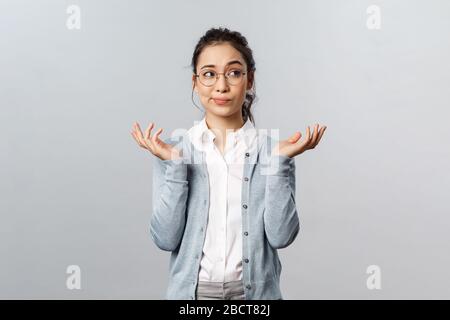 Lifestyle-, Menschen- und Emotionskonzept. Wer weiß. Portrait der unentschlossen zweifelhaften jungen asiatischen Frau, die brünette, mit dem Schrugging, der wegschaut und schwelgt Stockfoto