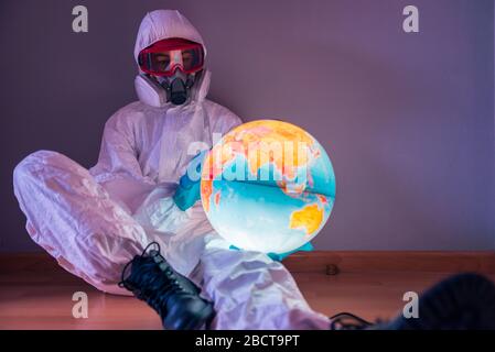 Konzept: Weltweite Viruskrise. Frau im Laborkittel, Nitrilhandschuhe, Brille, Gesichtsmaske und NBC-Anzug für Covid-19 Coronavirus, auf dem Boden von ihr sitzend Stockfoto