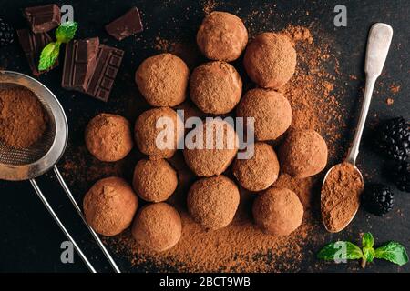 Schokoladentrüffel mit Kakaopulver auf schwarzem Schiefergrund. Tabellenansicht von oben. Hausgemachte Schokoladenbonbons Stockfoto